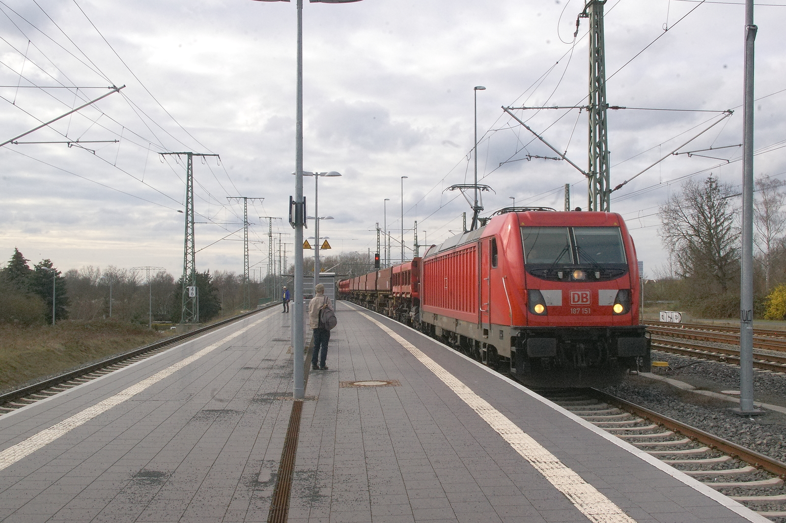 DB Cargo 187 151 fährt mit einem Schotterzug am 22.03.2023 durch den S-Bahnhof Thekla. Auf dem linken Gleis halten die S-Bahnzüge der S-Bahn Mitteldeutschland [91 80 6187 151-6 D-DB]
